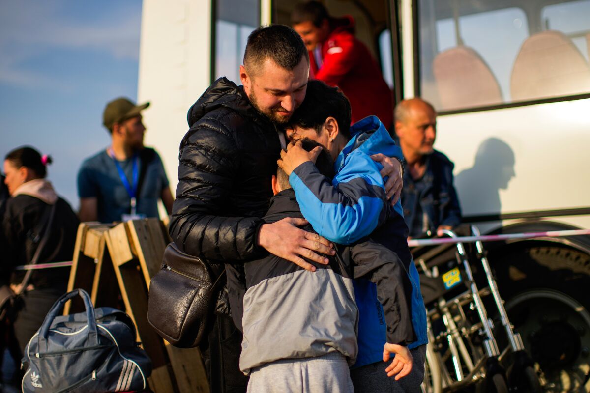 A woman hugs a man and a child near a bus