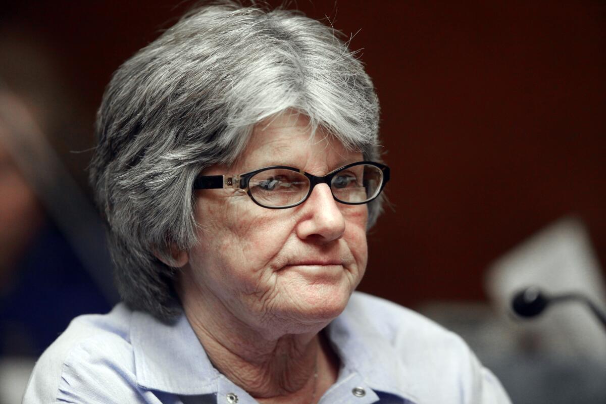 A closeup of a female inmate with glasses and graying hair seated at a microphone.