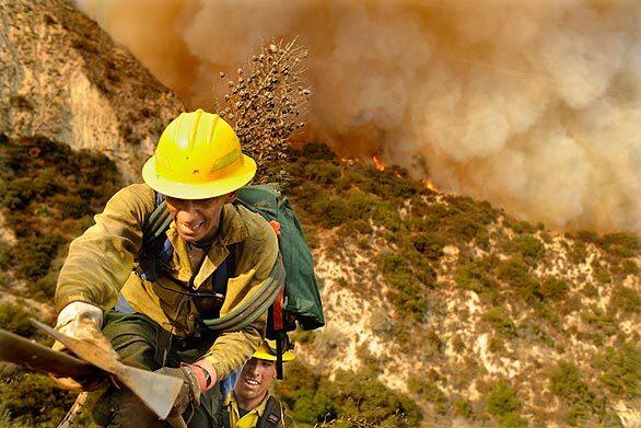 A Forest Service firefighter uses a fire hose to retreat from the approaching flames.