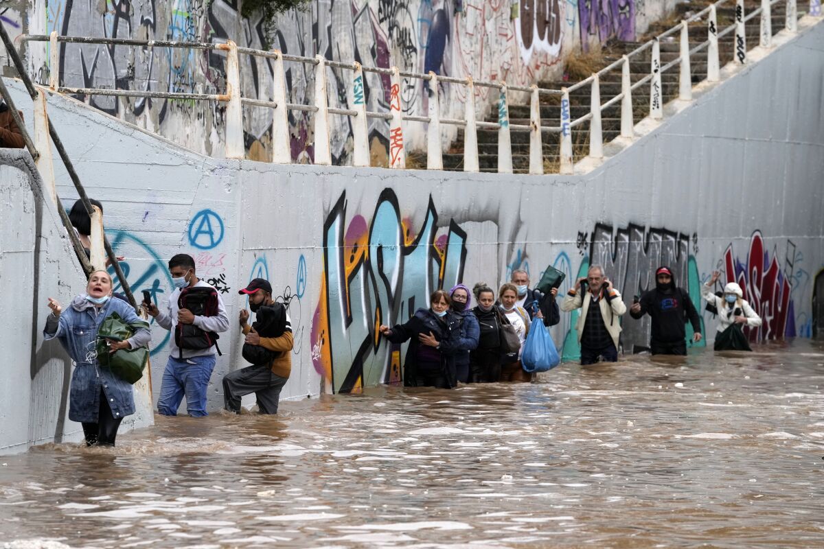 Passengers wade through high water after evacuating a bus stuck in a flooded underpass in southern Athens, Thursday, Oct. 14, 2021. Storms have been battering the Greek capital and other parts of southern Greece, causing traffic disruption and some road closures. (AP Photo/Thanassis Stavrakis)