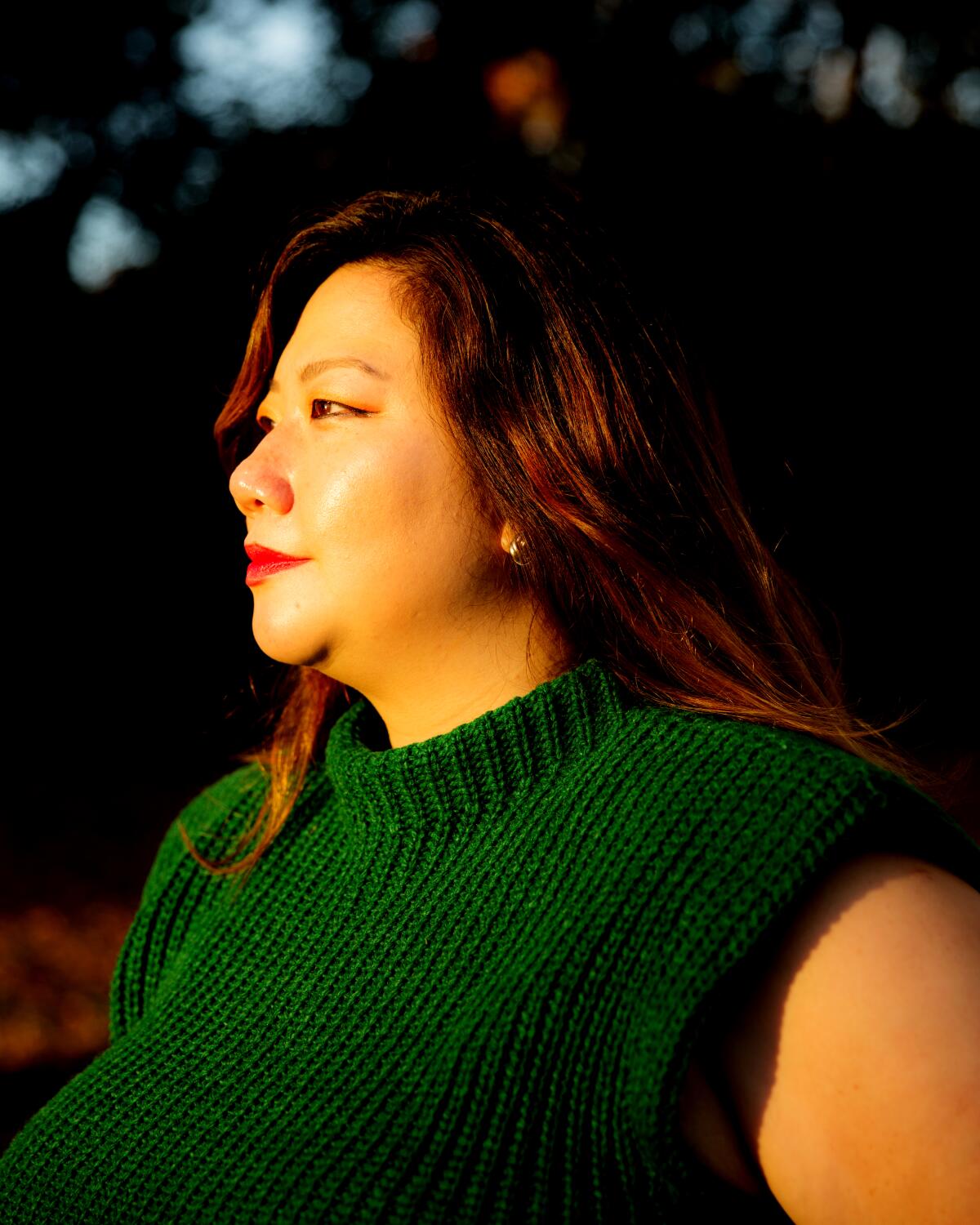 A woman in sunlit profile in a green sleeveless sweater.