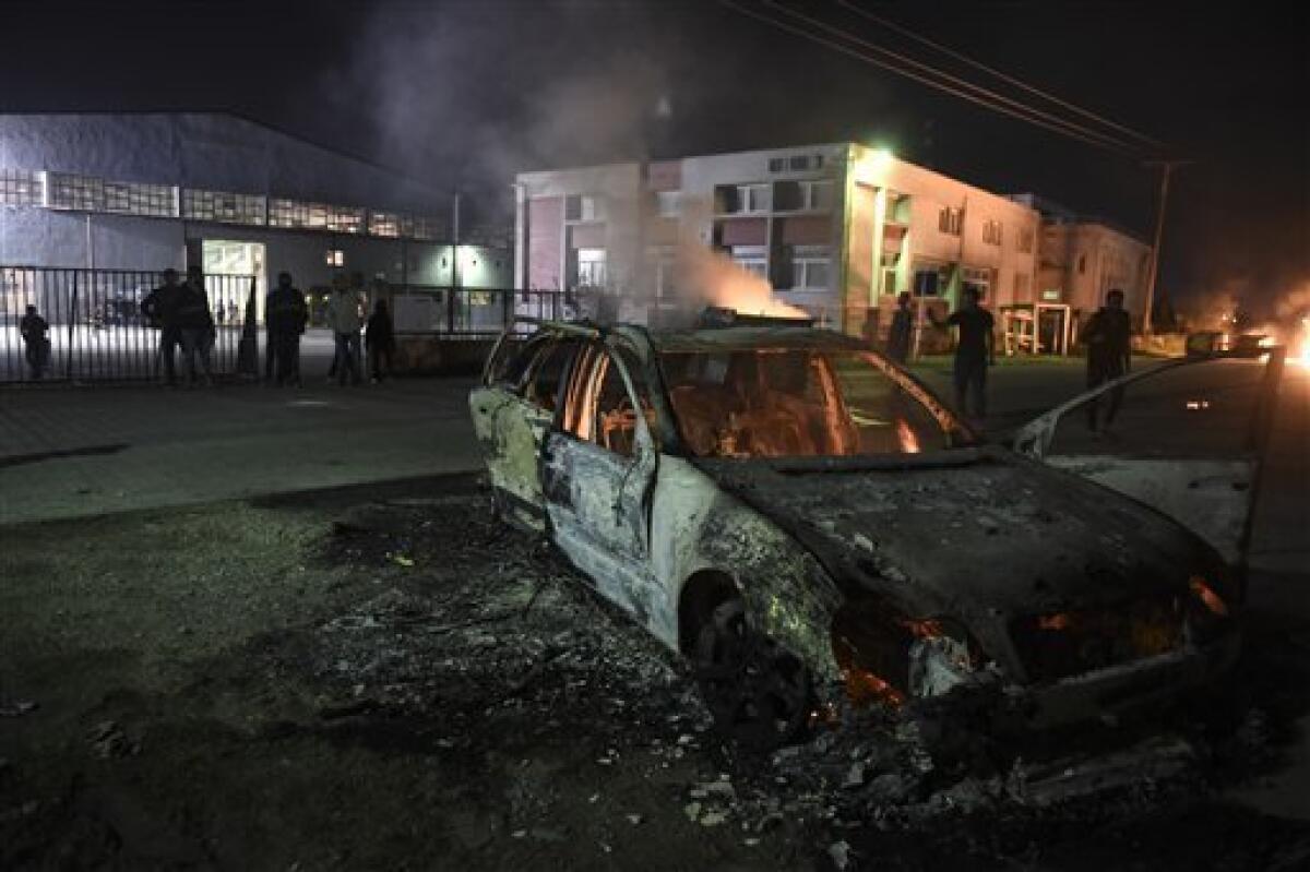 Un grupo de migrantes observa los restos de un vehículo incendiado afuera del campamento para refugiados de Oreokastro, cerca del poblado de Tesalónica del norte de Grecia, el domingo 16 de octubre de 2016.