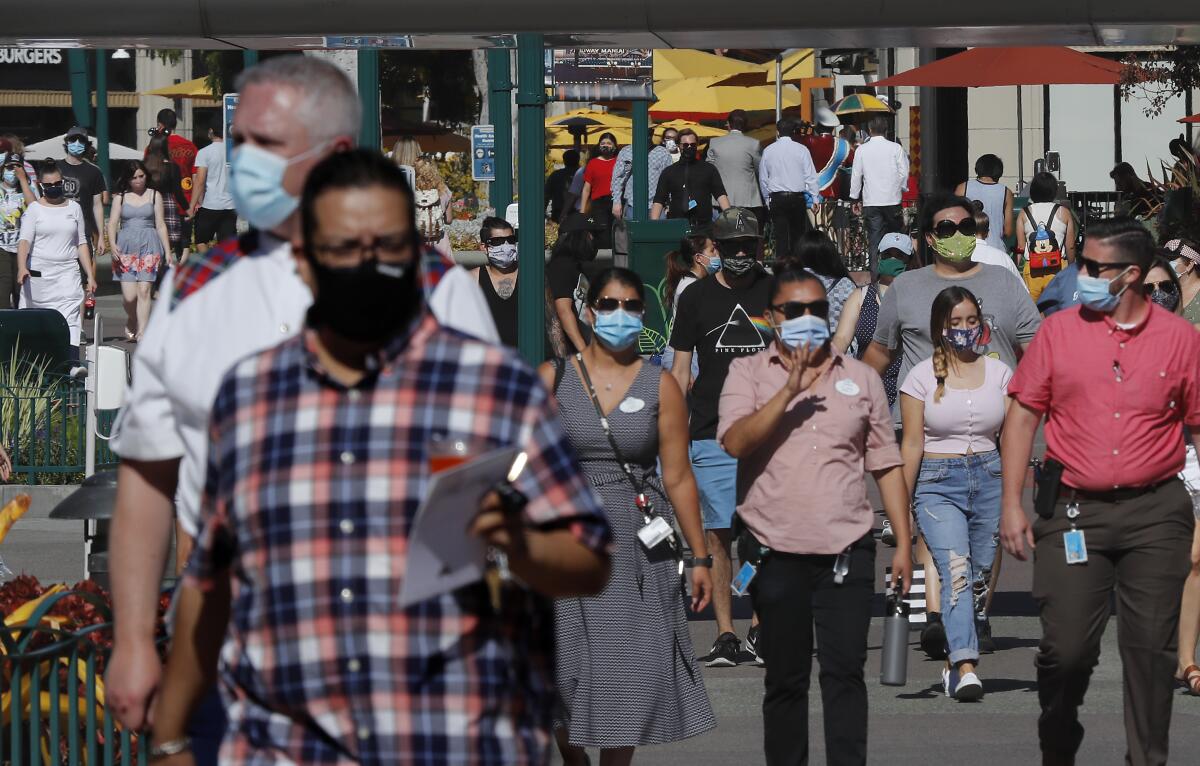 Scores of visitors wearing masks walk through Downtown Disney in Anaheim for its reopening