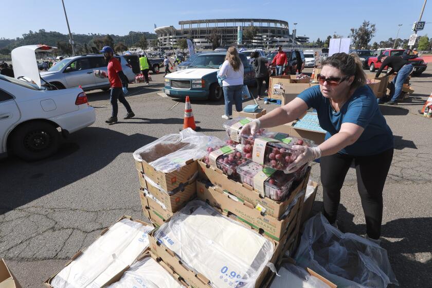 Deanna Wallace opens up boxes of grapes as fellow volunteers place food items into the trunks of people's cars during the Mass Emergency Food Distribution, put on by the San Diego and Imperial counties Labor Counsel and the San Diego Food Bank, at SDCCU Stadium on Saturday March 28, 2020 in San Diego, California.