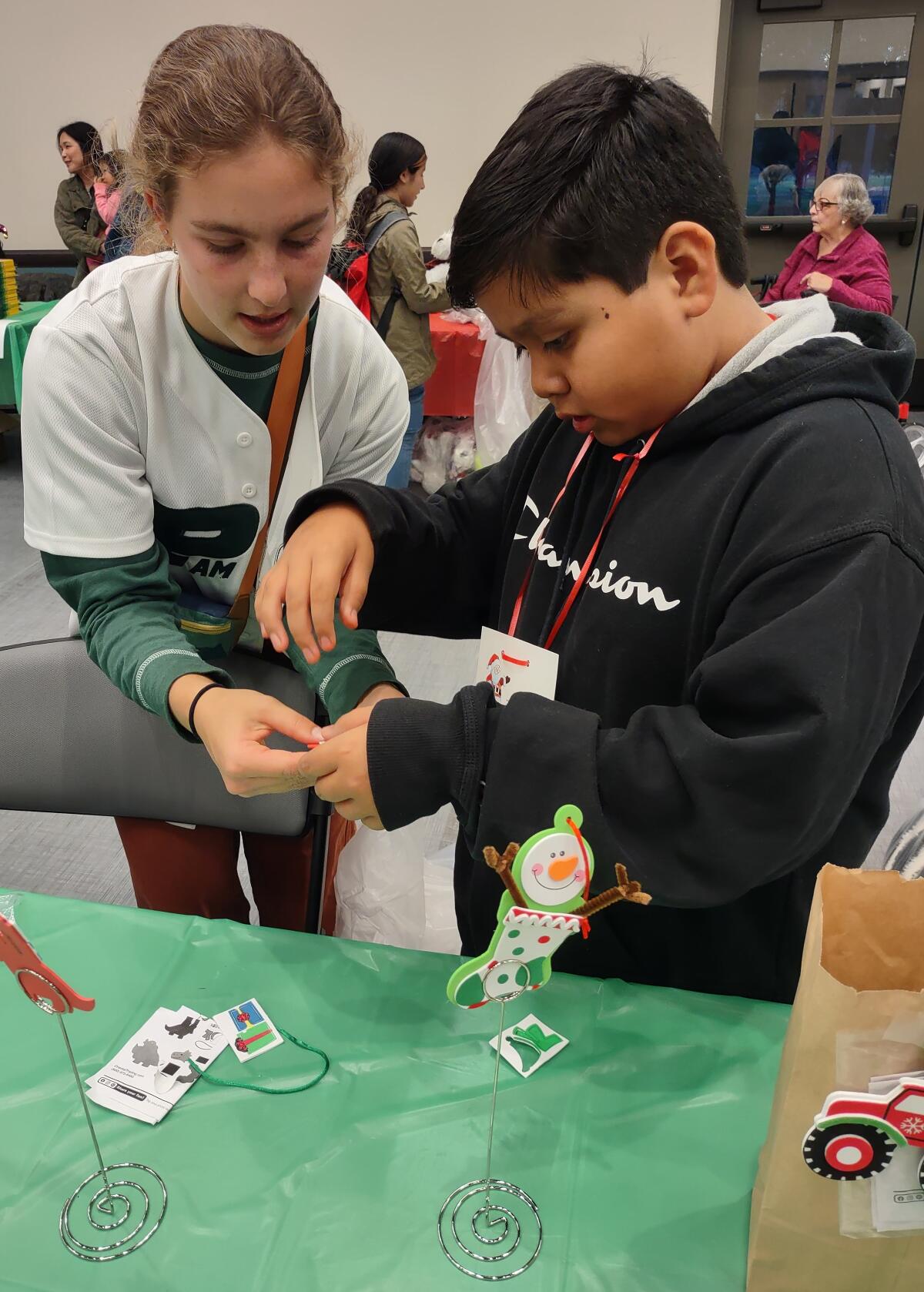 Anjolie Norton helps Jose Martinez make a dinosaur Christmas tree ornament.