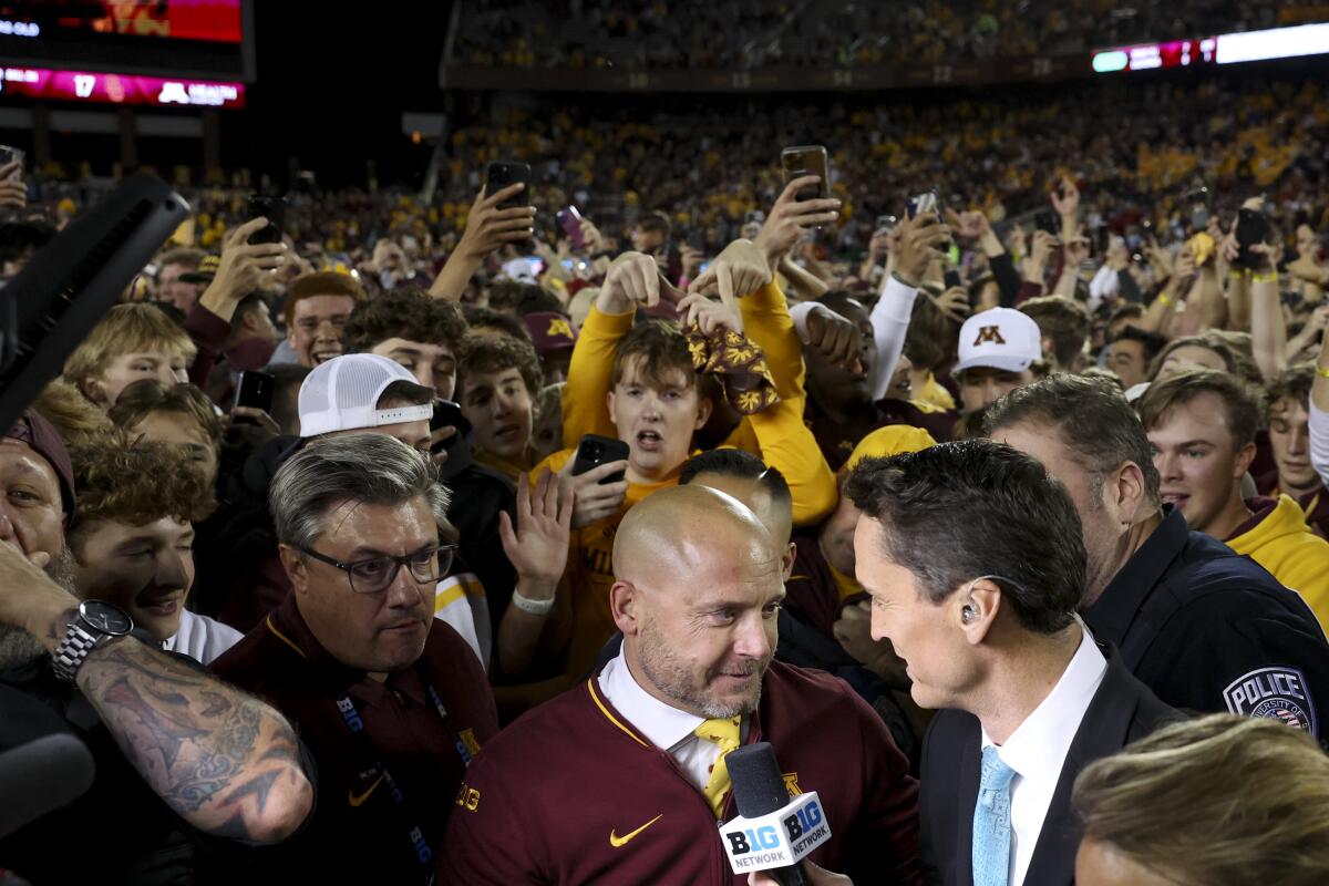 Minnesota koçu PJ Fleck, taraftarlar ona akın ederken bir muhabirle konuşuyor 