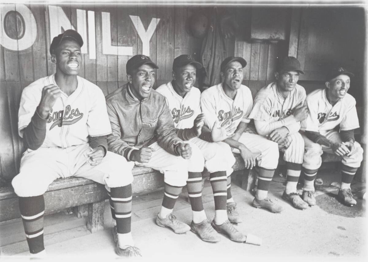 Six baseball players on the bench react to a play in an old black and white photo.