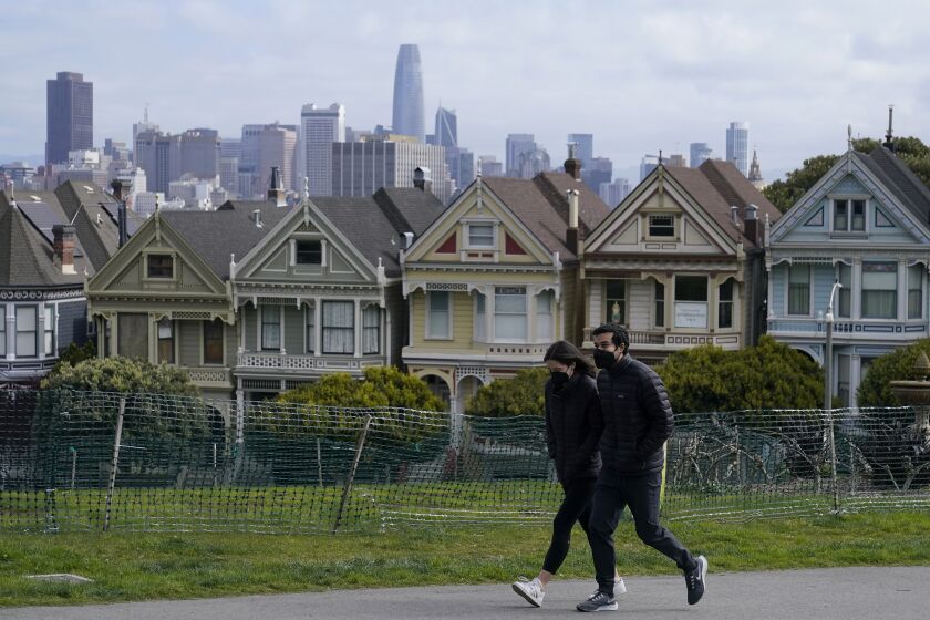 FILE - In this March 13, 2021, file photo, people wearing masks walk along at path in front of the "Painted Ladies," a row of historical Victorian homes, and the San Francisco skyline at Alamo Square Park during the coronavirus pandemic in San Francisco. California will offer six "dream vacation" incentives to spur more people to get coronavirus vaccinations, California Gov. Gavin Newsom said Monday, June 14, 2021, on the eve of the state's awarding of $15 million in cash prizes. Newsom spoke in San Francisco, site of one of the six vacation packages offered by various providers through Visit California, the state's quasi-independent travel promotion arm. (AP Photo/Jeff Chiu, File)