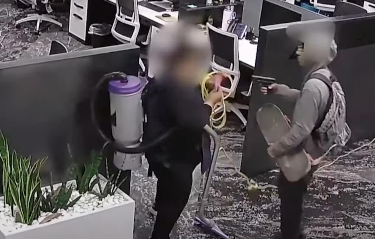 A man points a replica gun at a woman in an office building.