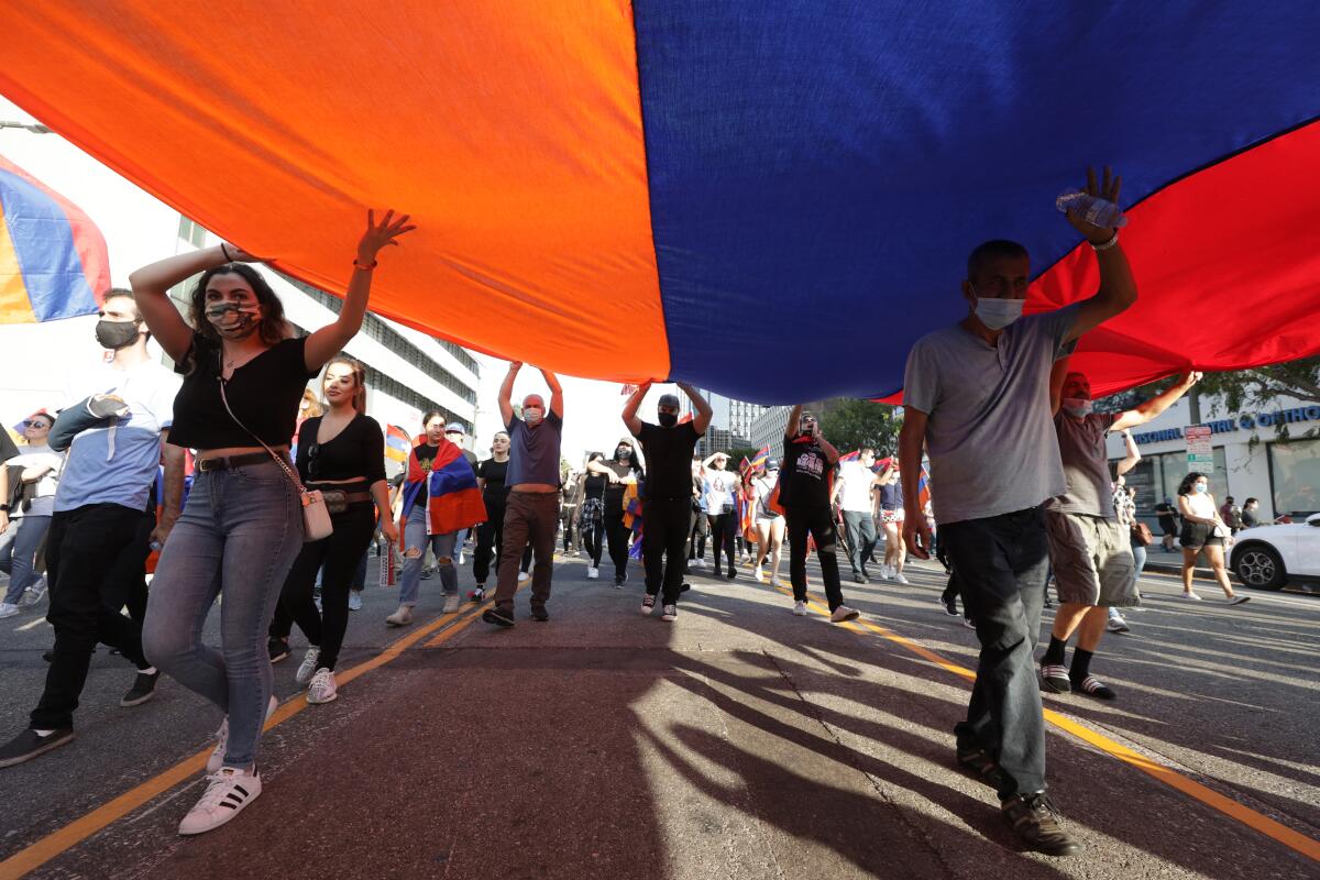 Protesters in the street carry a giant red blue and orange Armenian flag above their heads