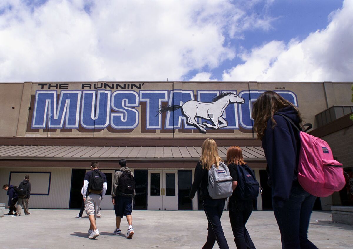 Students on an outdoor campus under a mural that reads The Runnin' Mustangs