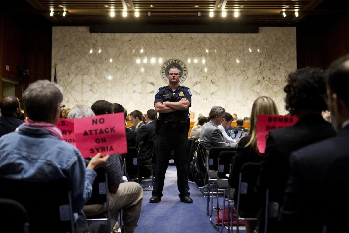 A Capitol Hill police officer watches as protesters hold signs reading "No Attack on Syria" during the Senate Foreign Relations Committee hearing on Syria on Capitol Hill in Washington.