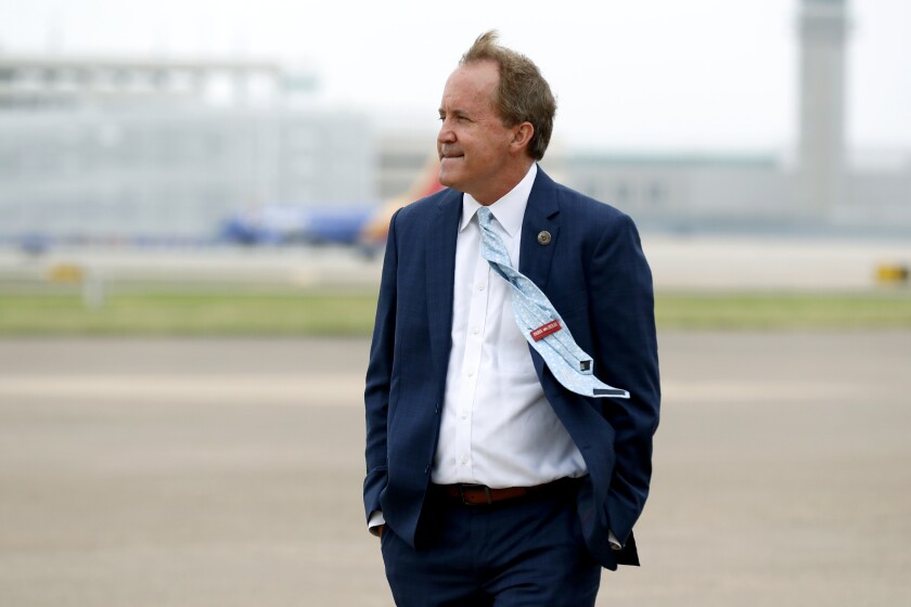 Ken Paxton stands with hands in pockets on an airport tarmac, his tie blowing in the wind.