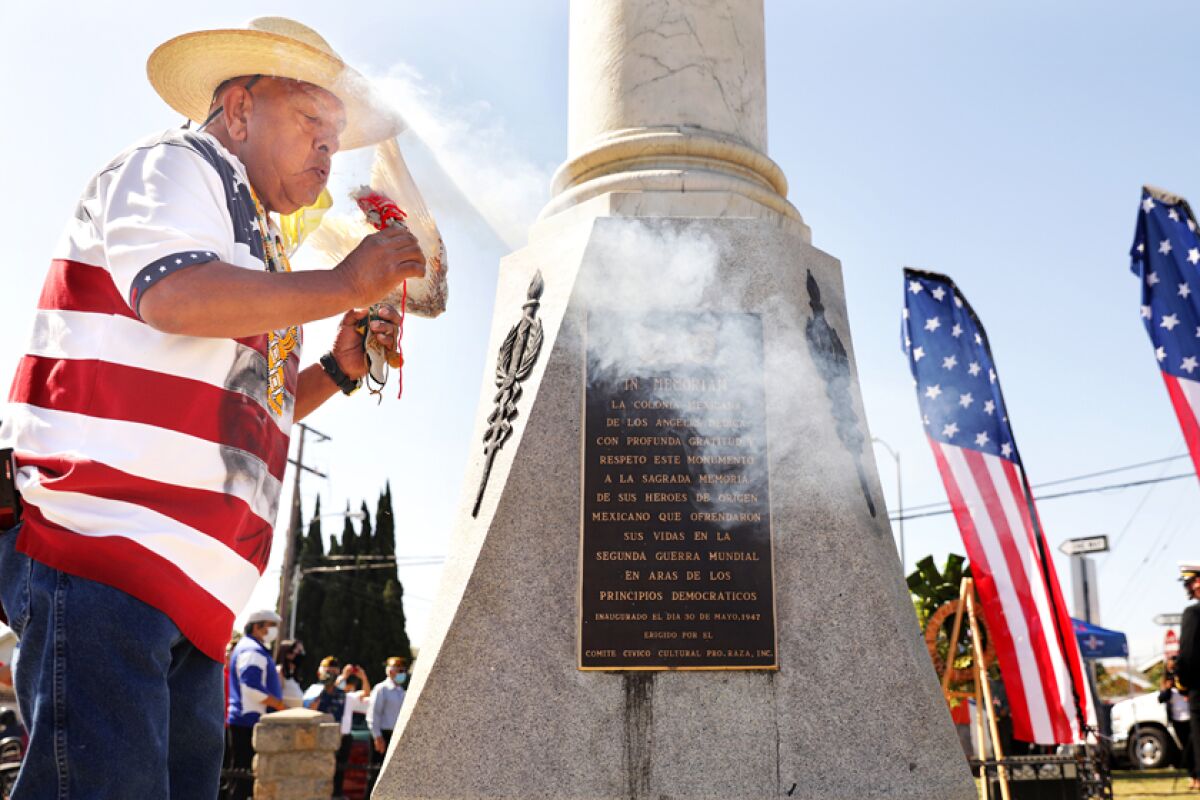A man blows on something that's smoking in front of a monument.