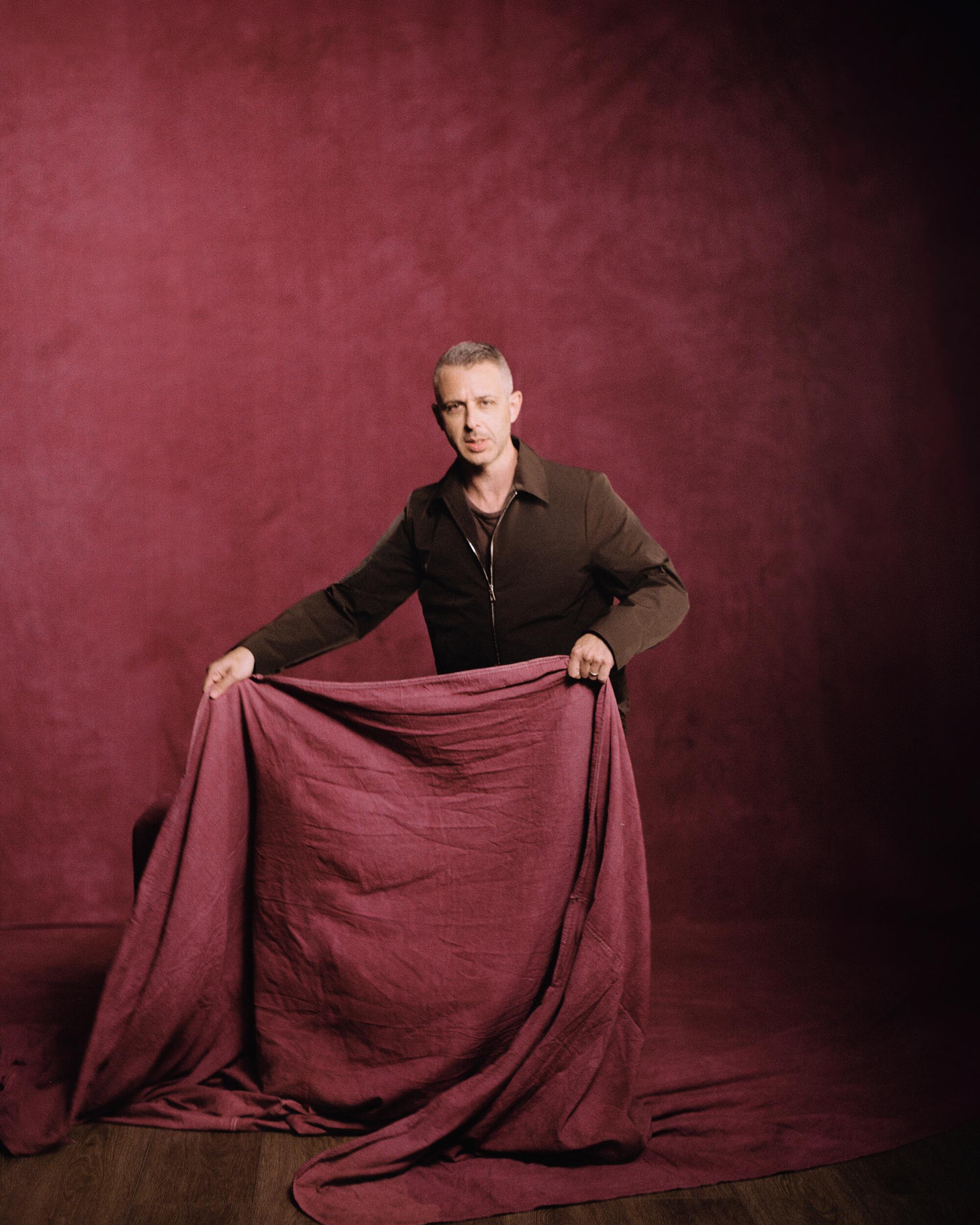 Actor Jeremy Strong in holds up a dropcloth like a matador's cape for a portrait.