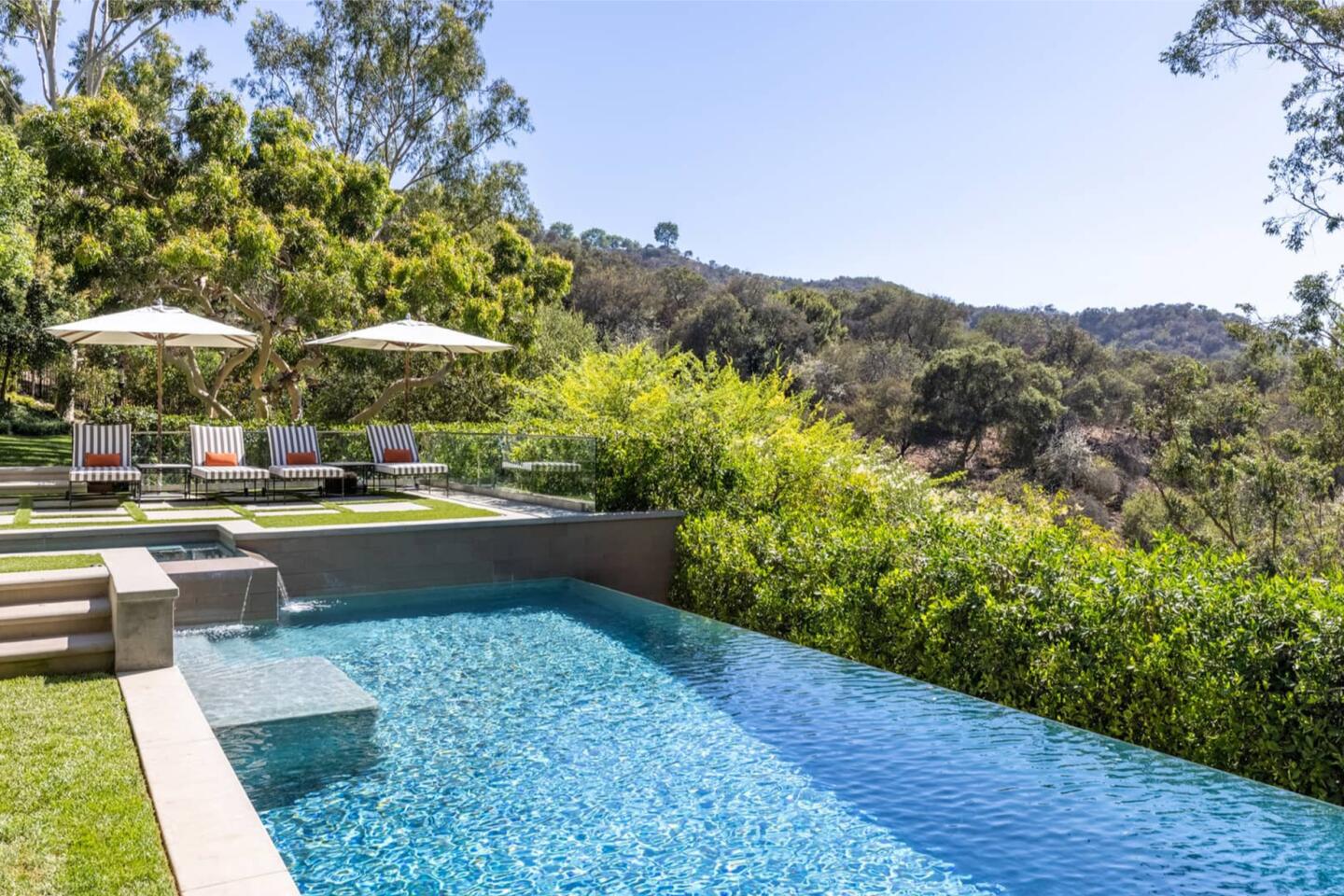 The pool has grass on one side and shrubs on the other side looking out over hills.