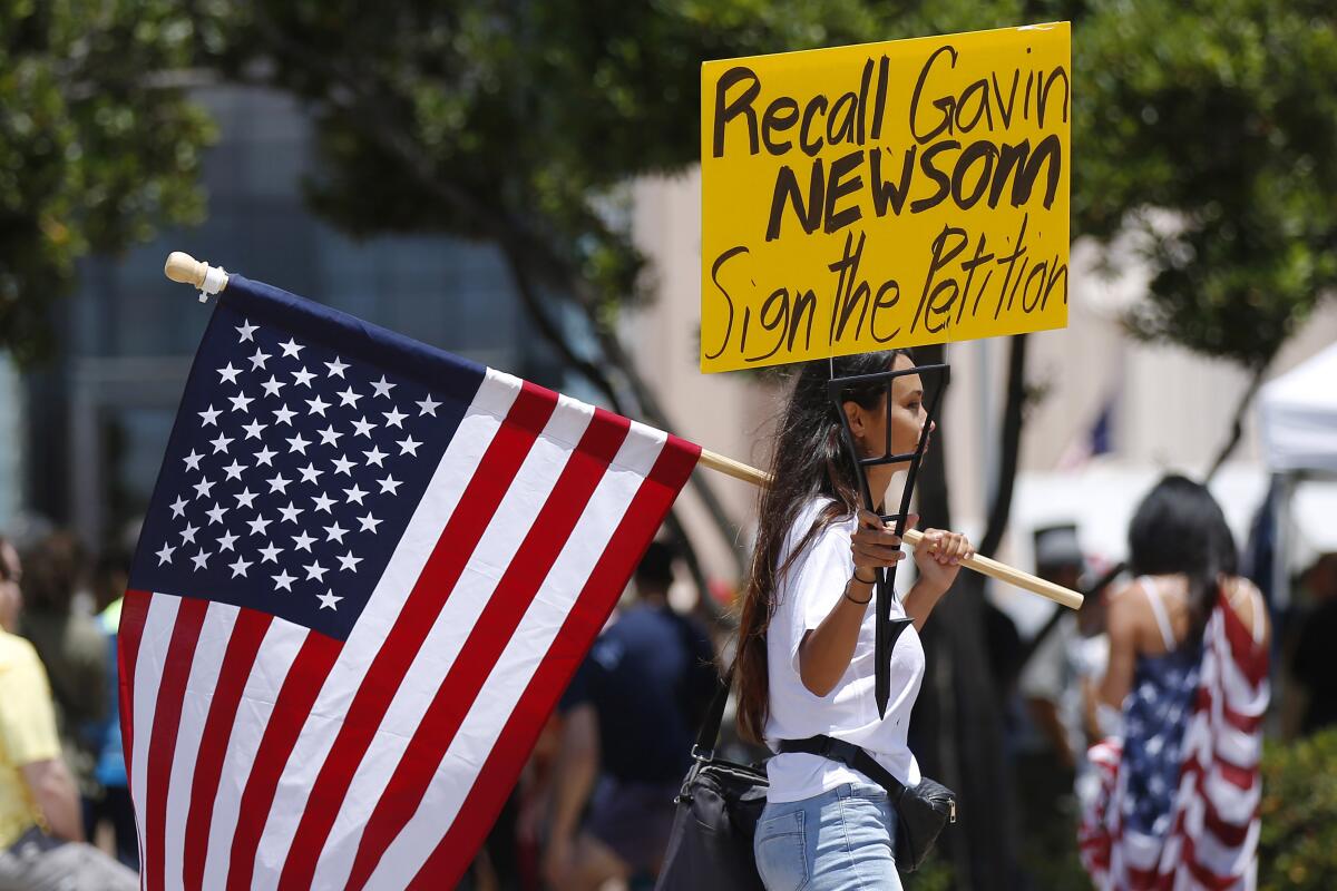 A protester holds an American flag and a "Recall Gavin Newsom" sign