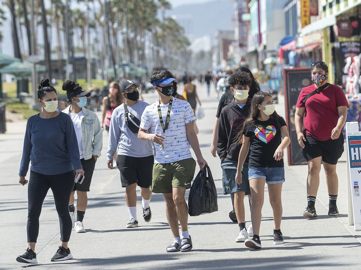 People wear masks to protect against the coronavirus while walking along the boardwalk in Venice Beach. A new rule, announced by Mayor Eric Garcetti on Wednesday, now requires face masks for all outdoor activities.