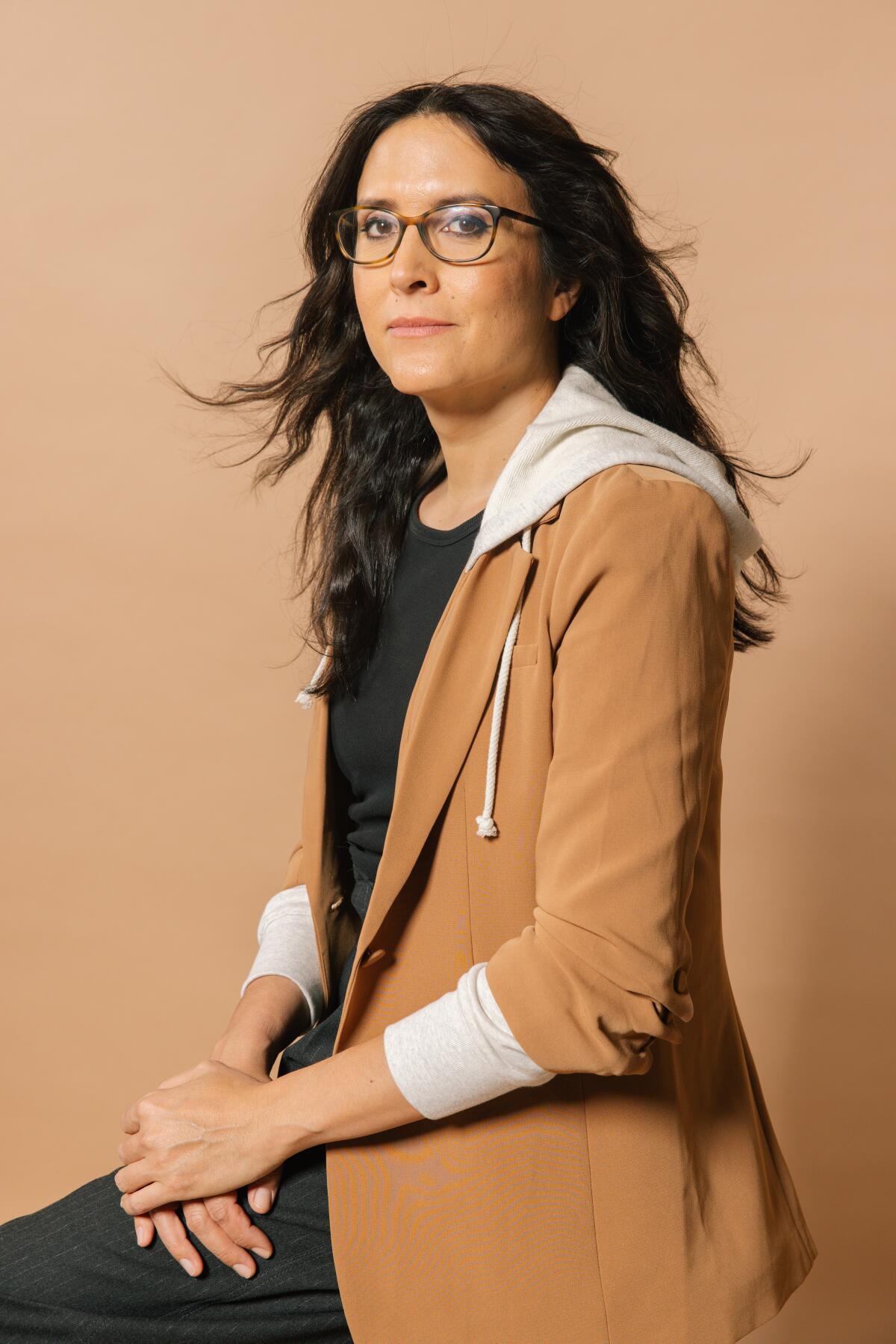 A woman with glasses and long hair looks at the camera.