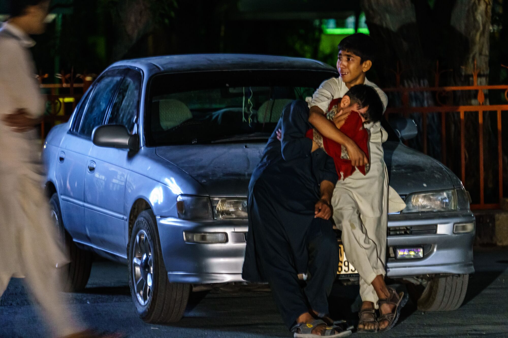 Two boys embrace each other  next to a car