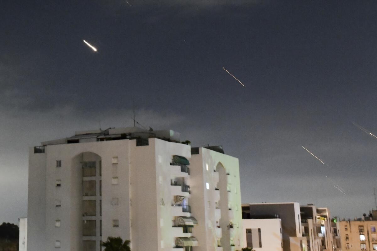 Missiles streak over buildings in the twilight sky.