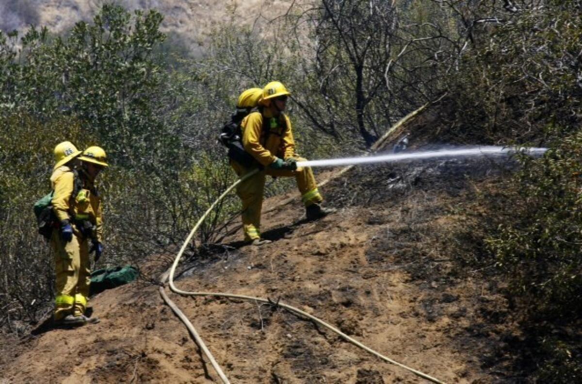 Firefighters douse the hillside in Burbank on Monday as they worked to contain a brush fire that started near DeBell Golf Club.
