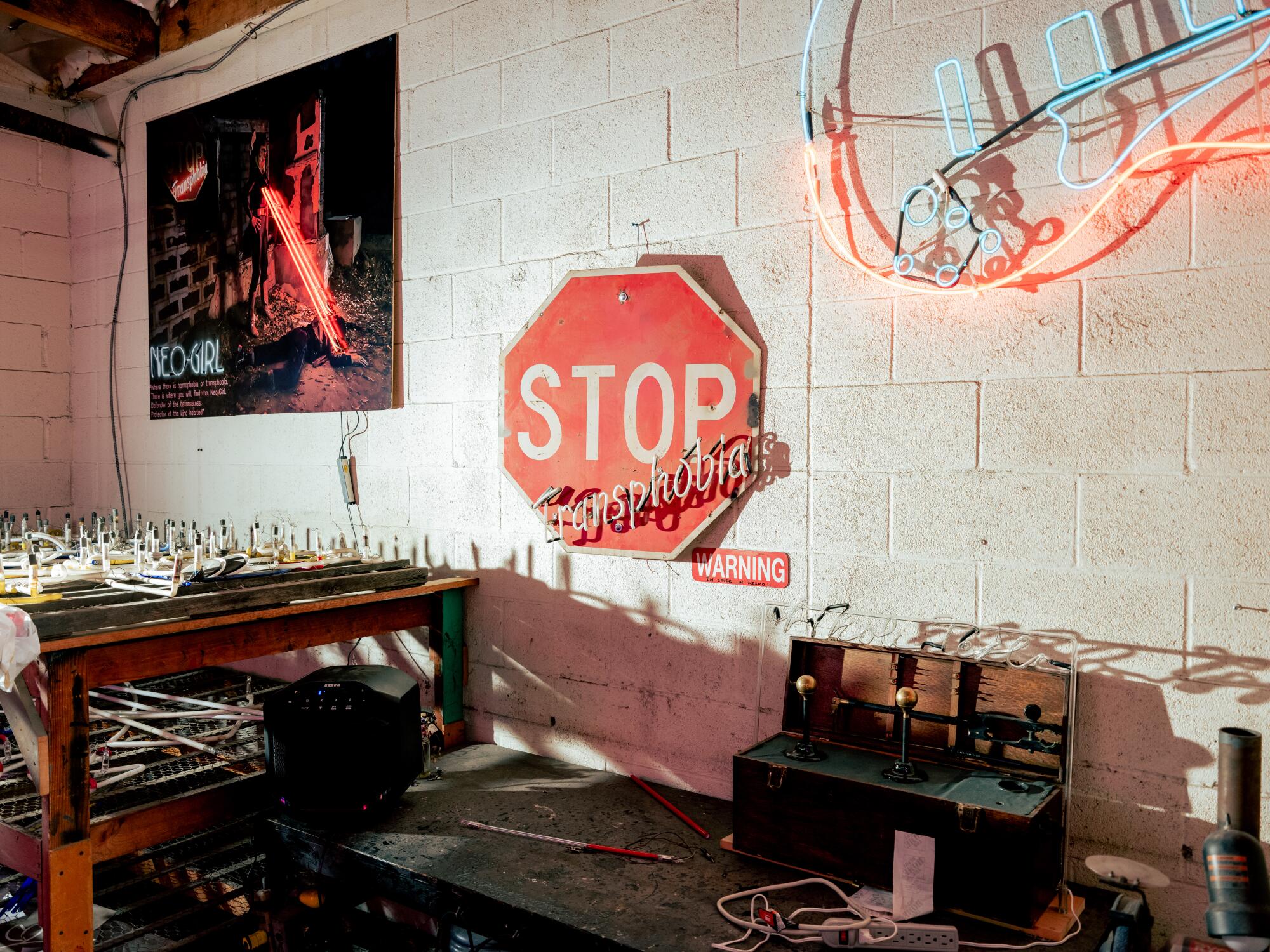 A red stop sign with an added word in neon so that it reads "Stop Transphobia" hangs on a cinderblock wall