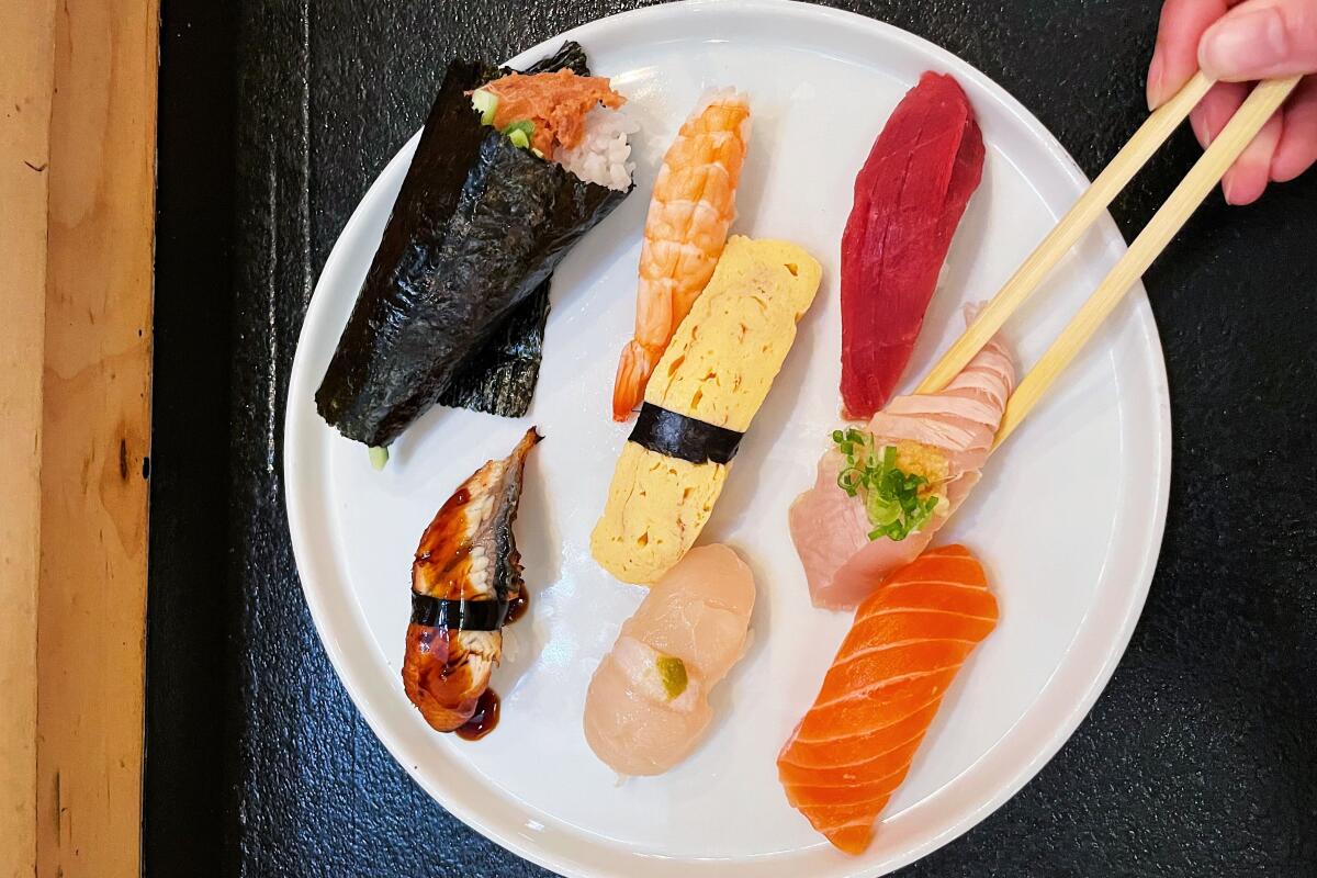An overhead photo of the sushi lunch special at Murakami Sushi on Melrose. A hand with chopsticks lifts nigiri from top right