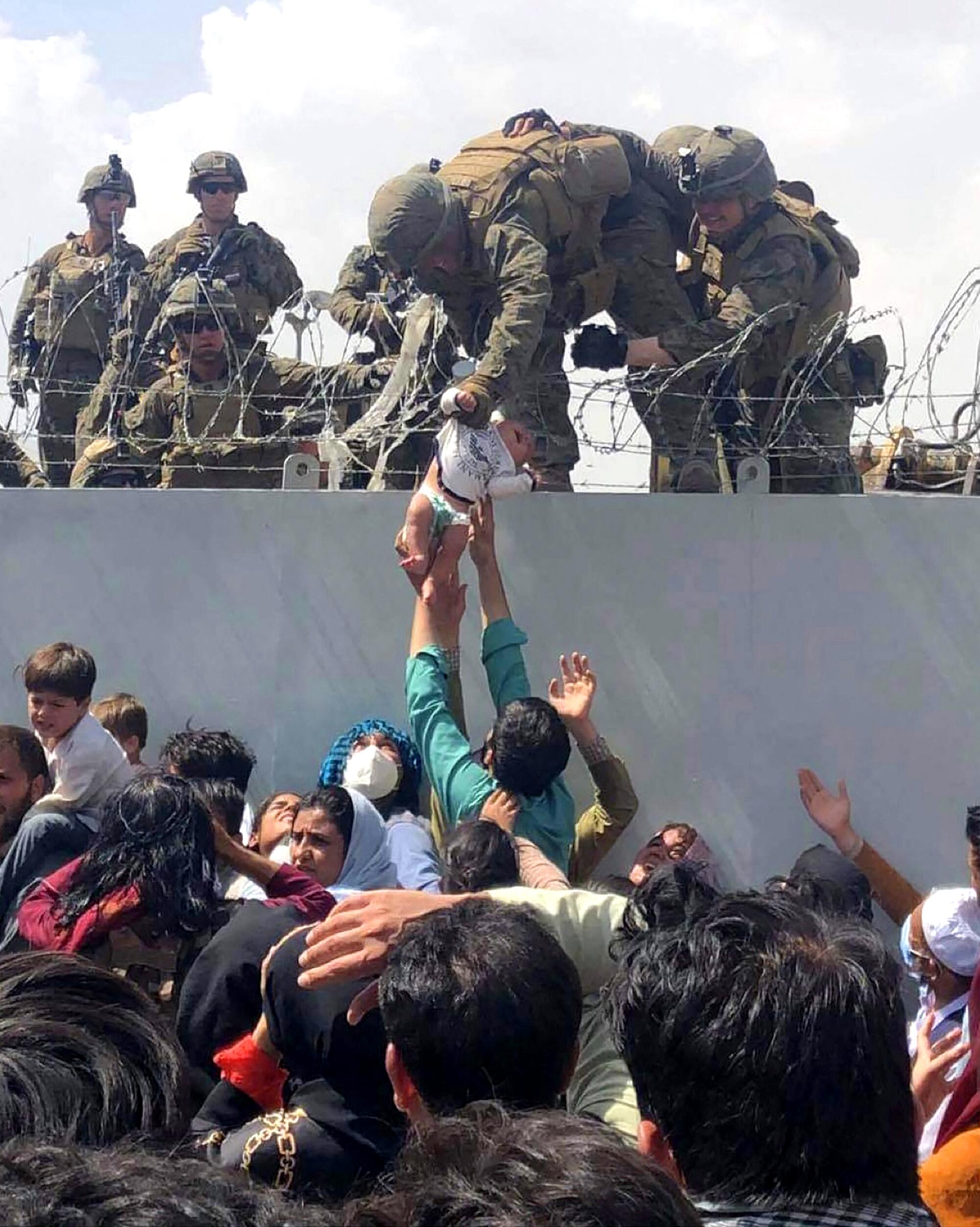 A man hands an infant up to a U.S. Marine over a barbed-wire fence