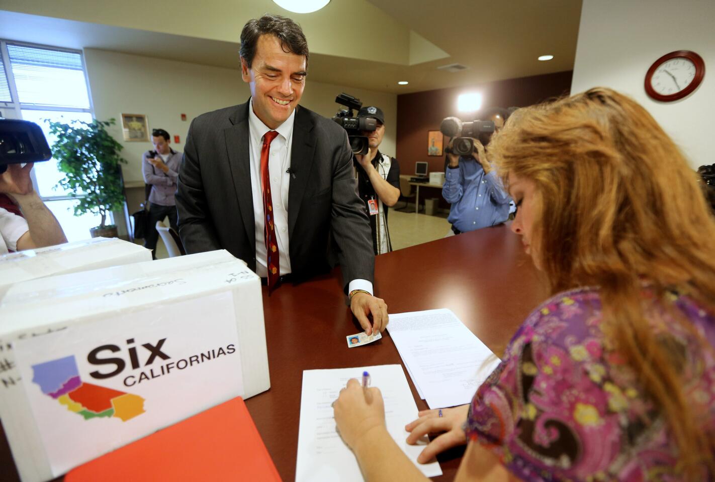 Silicon Valley venture capitalist Tim Draper presents his driver's license to Heather Ditty, elections manager for the Sacramento County Registrar of Voters, as he turns in boxes of petitions for a ballot initiative that would ask voters to split California into six separate states.