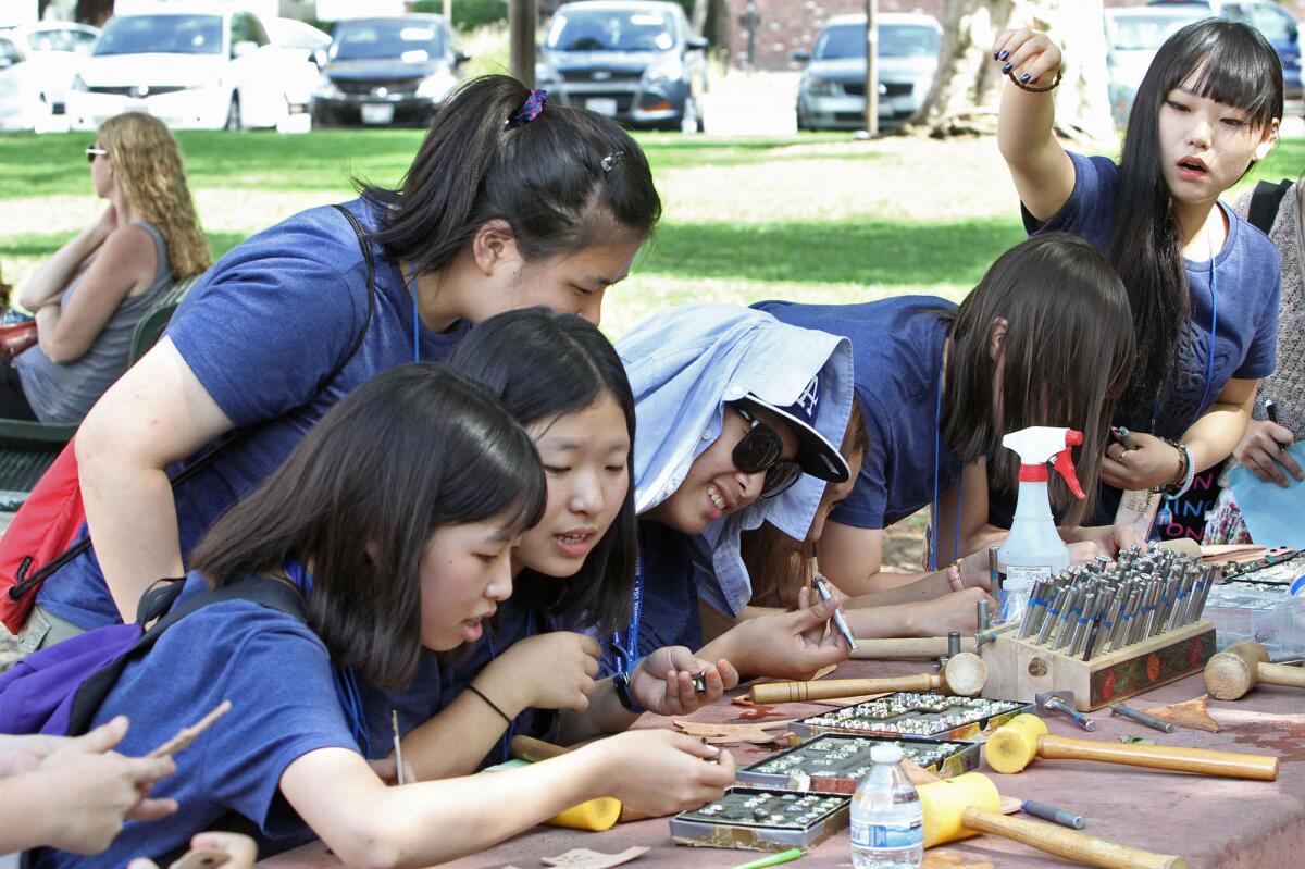 Visiting high school and college students from Incheon, South Korea, try their hand doing leather work at Ralph Foy Park on Monday, July 28, 2014.