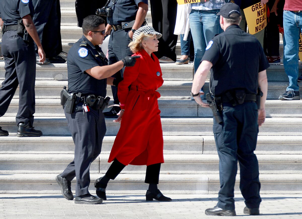 Jane Fonda, with hands cuffed behind her back, being led by a police officer near the Capitol steps.