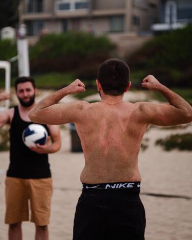 Two beach volleyball players face each other, holding their bent arms up to make muscles
