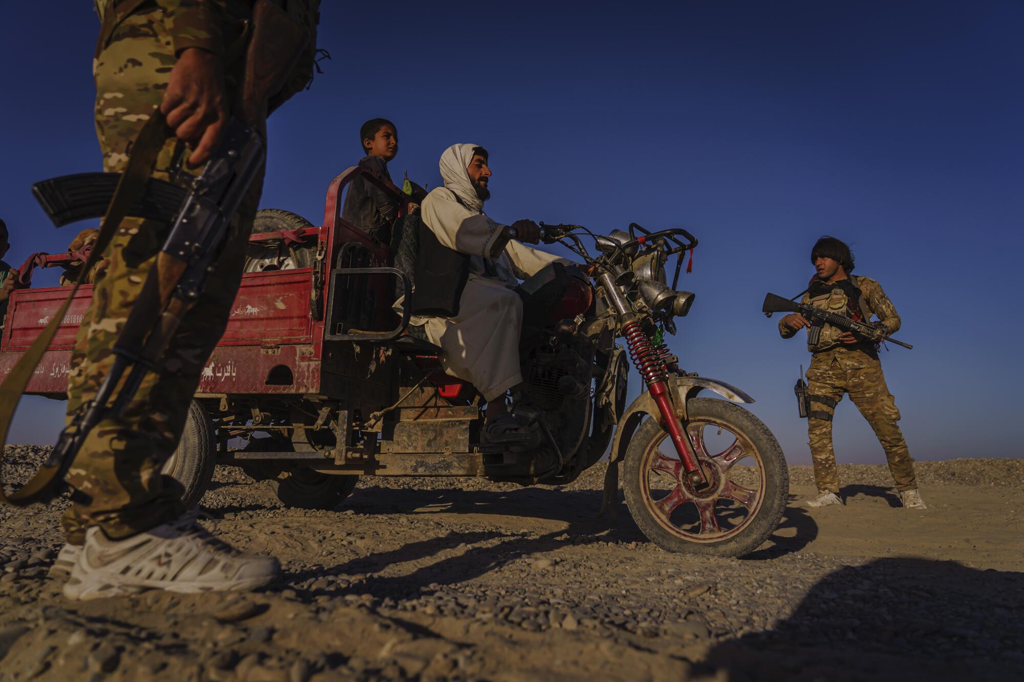 Afghan police officers in sneakers and camouflage talk to two people on a three-wheel vehicle.