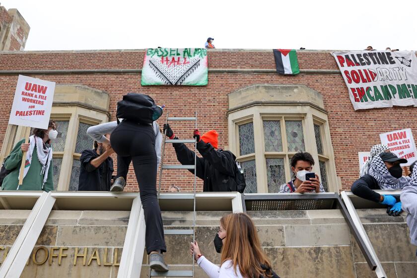 LOS ANGELES-CA-MAY 23, 2024: UCLA protestors climb up a ladder at Kerckhoff Hall as they try to build a new Palestinian solidarity encampment on campus on May 23, 2024. (Christina House / Los Angeles Times)