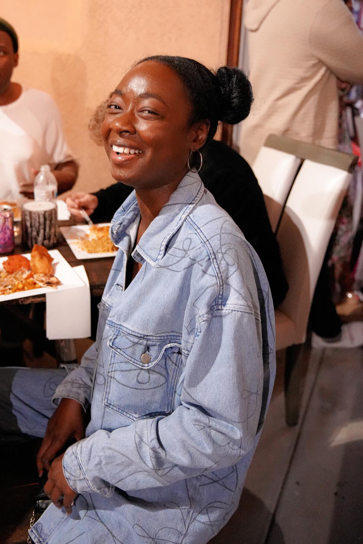 A young woman dressed in a jean jacket, smiling.