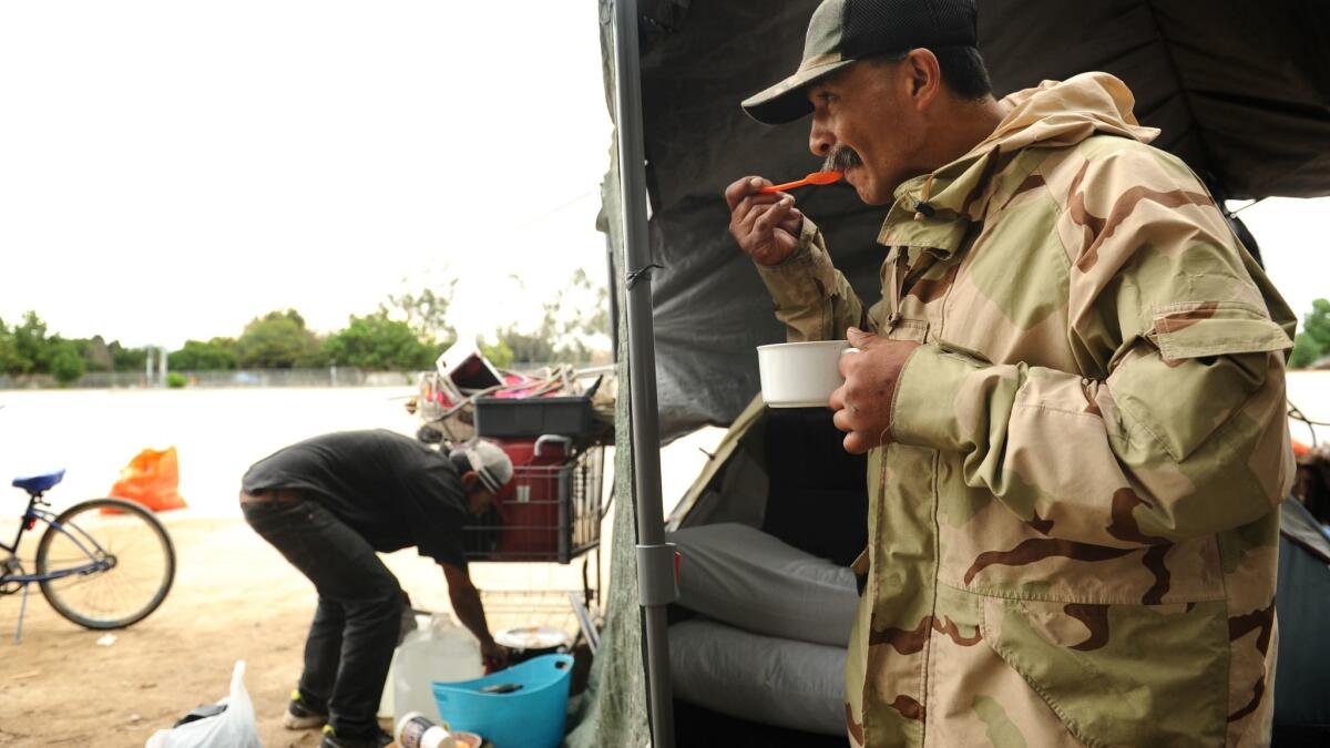 Sergio Guerra eats a bowl of cereal for breakfast as his cousin, Rigo Alijas, cleans up around their living space. Officials announced plans to close the homeless encampment along the Santa Ana River in Fountain Valley.