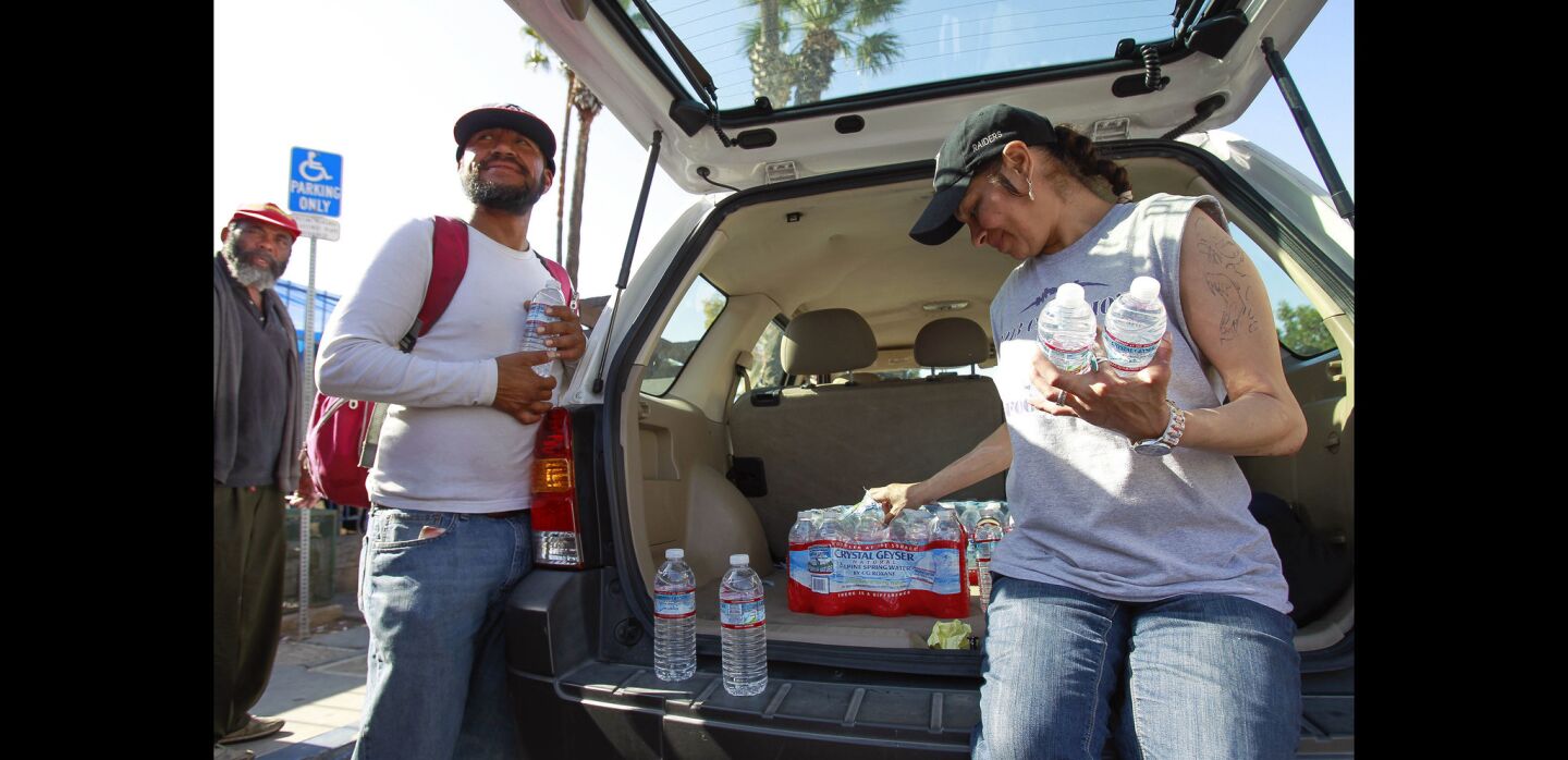 Mary Ellen Paredez, right, helps distribute bottled water to other homeless people from the back of Dave Ross's car on 17th Street.