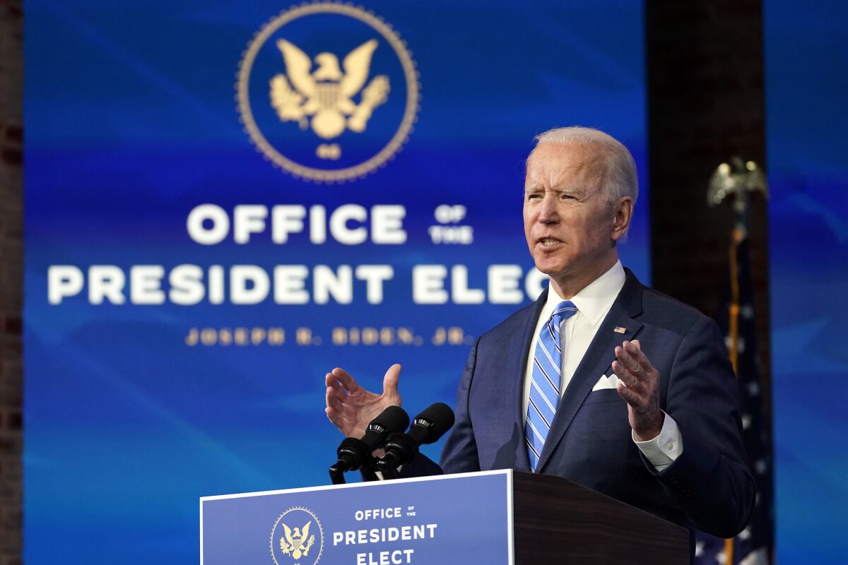 President-elect Joe Biden gestures while speaking at a lectern in front of a screen that says Office of the President Elect