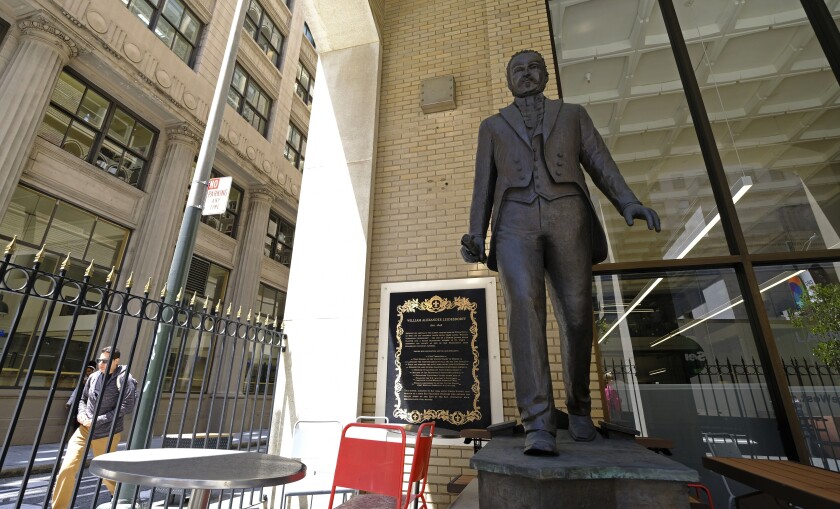 A statue of a man, with a nearby plaque, on a city street.