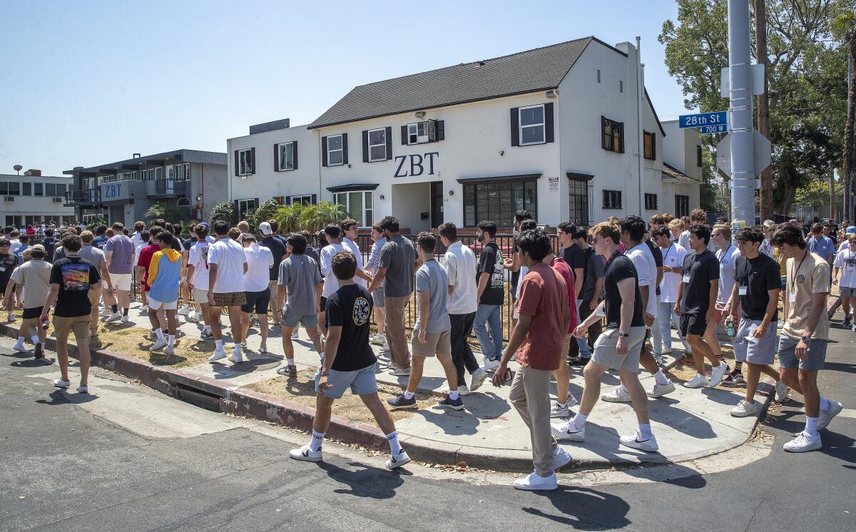 A crowd of young men walk past fraternity houses