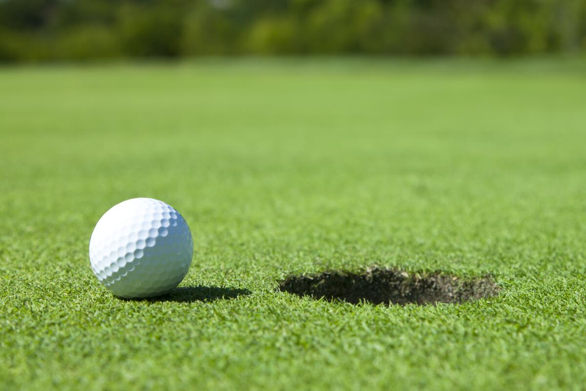 A golf ball sits next to a golf hole on the ground.