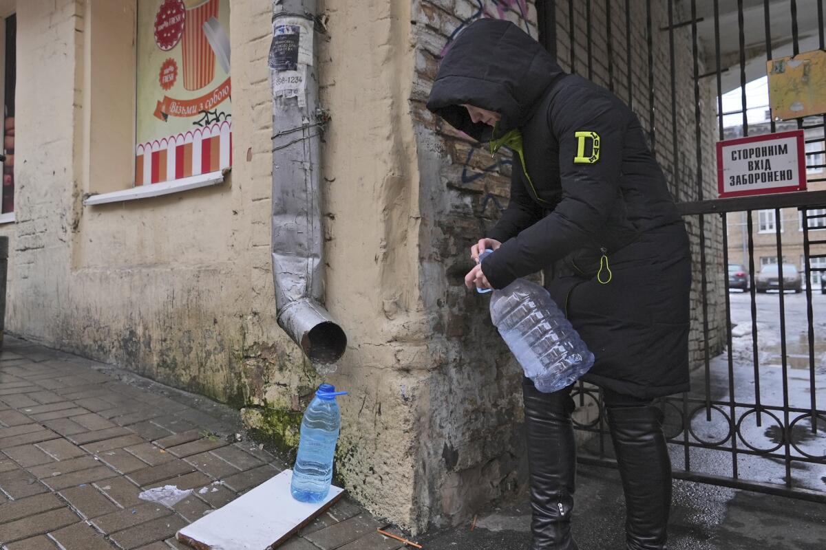 Woman collecting rainwater from a drainpipe in Kyiv, Ukraine