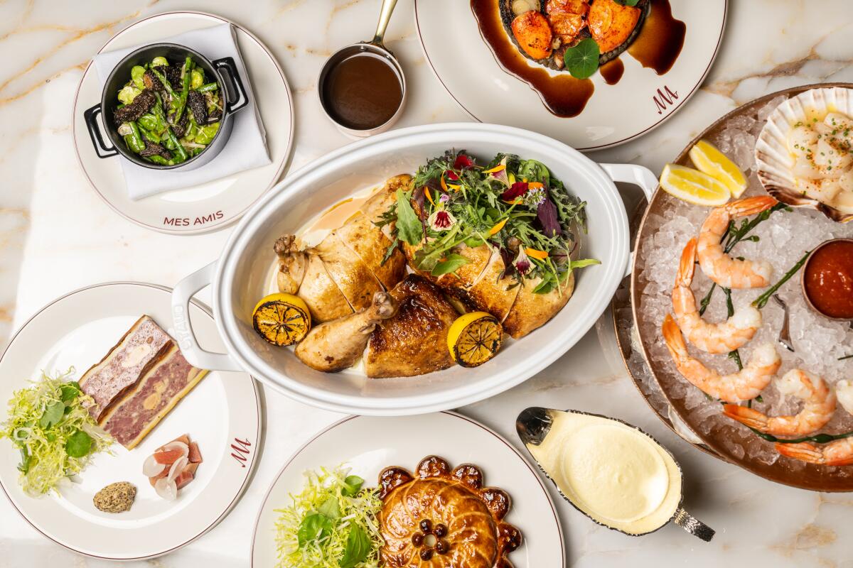 Platters and plates of food on a marble tabletop including shrimp on ice and sliced chicken.