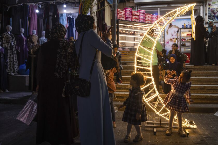 A Palestinian woman takes photos of her daughter next to a crescent moon-shaped decoration in a market, at the beginning of the Muslim holy month of Ramadan in Jebaliya refugee camp, northern Gaza Strip, Wednesday, March 22, 2023. (AP Photo/Fatima Shbair)