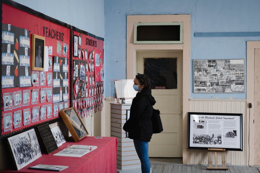 A woman in a dark jacket and jeans looks at photos on a wall display with a red back 