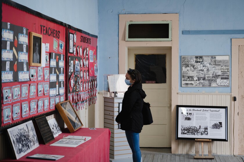 A woman in a dark jacket and jeans looks at photos on a red-backed wall display