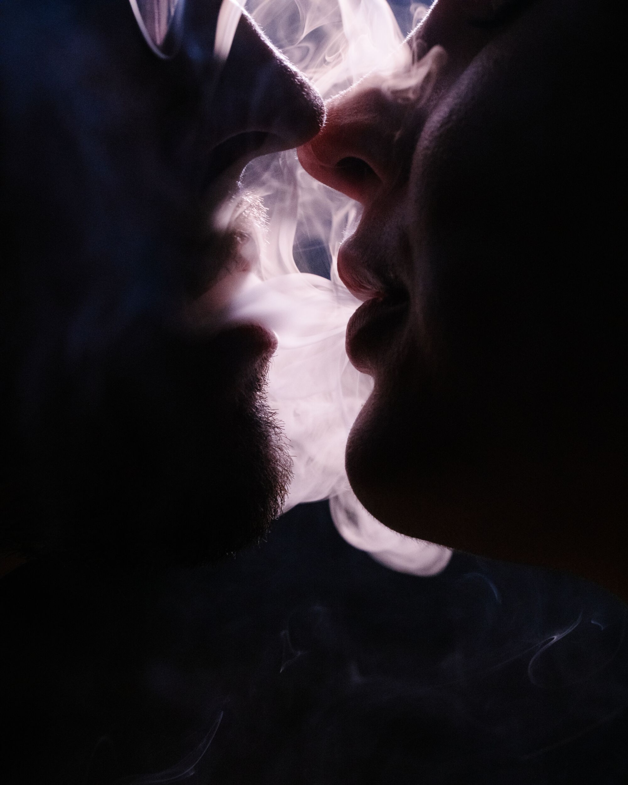 Two people smoke weed as they are about to kiss.
