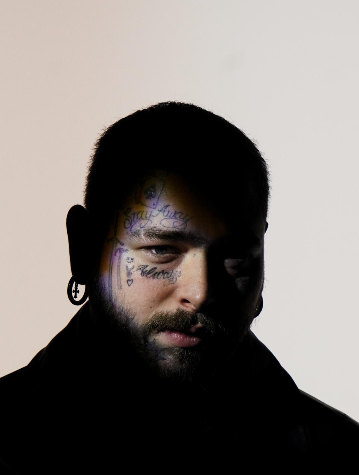 A man with short cropped hair, beard and face tattoos