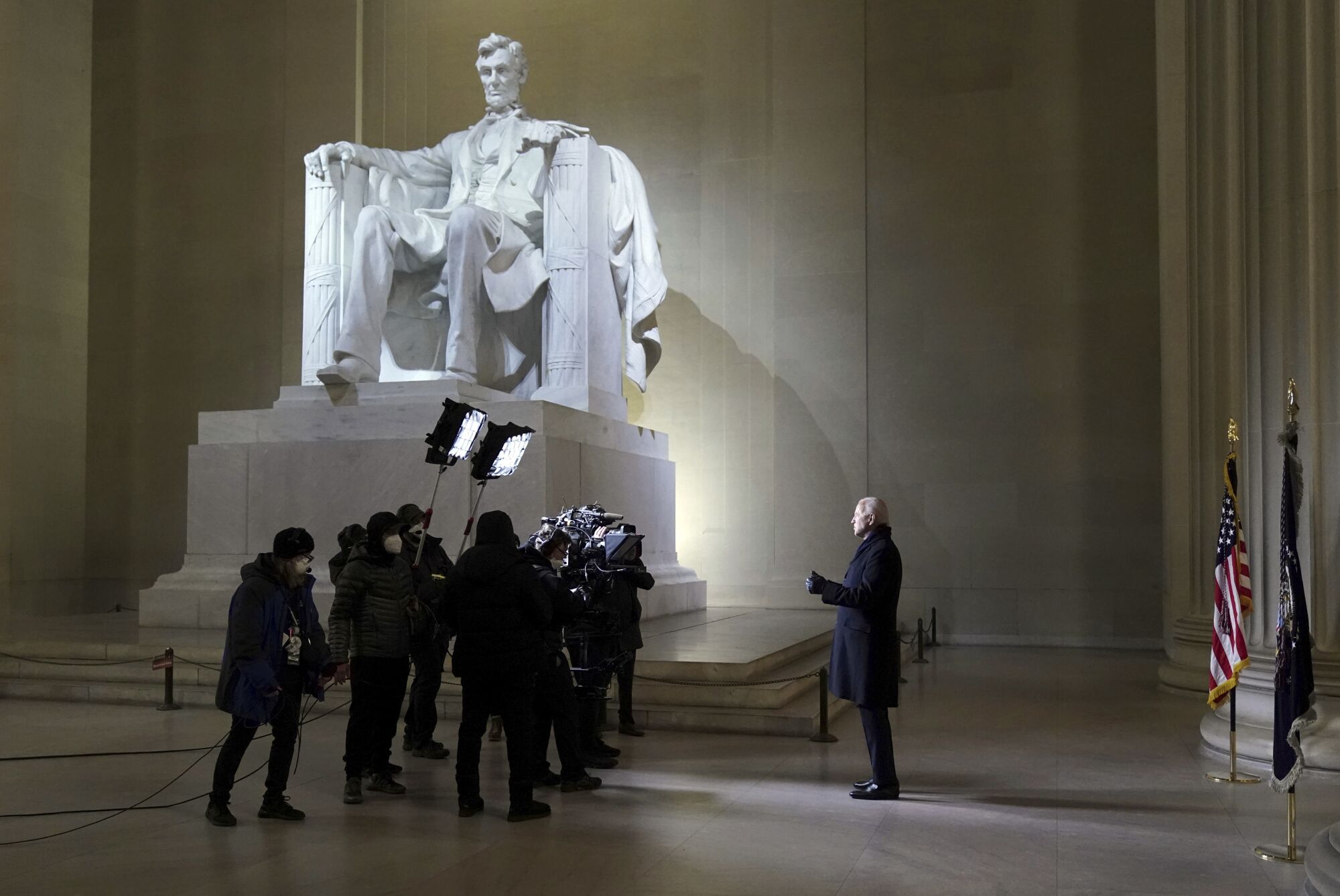President Biden stands alongside the Lincoln Memorial with a small crowd of reporters and TV camera operators.